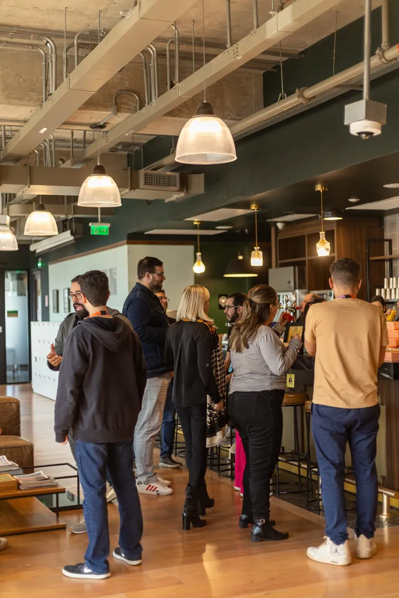 Grupo de pessoas reunidas em pé num lounge corporativo, conversando ao redor do balcão de atendimento Caixa Gourmet.