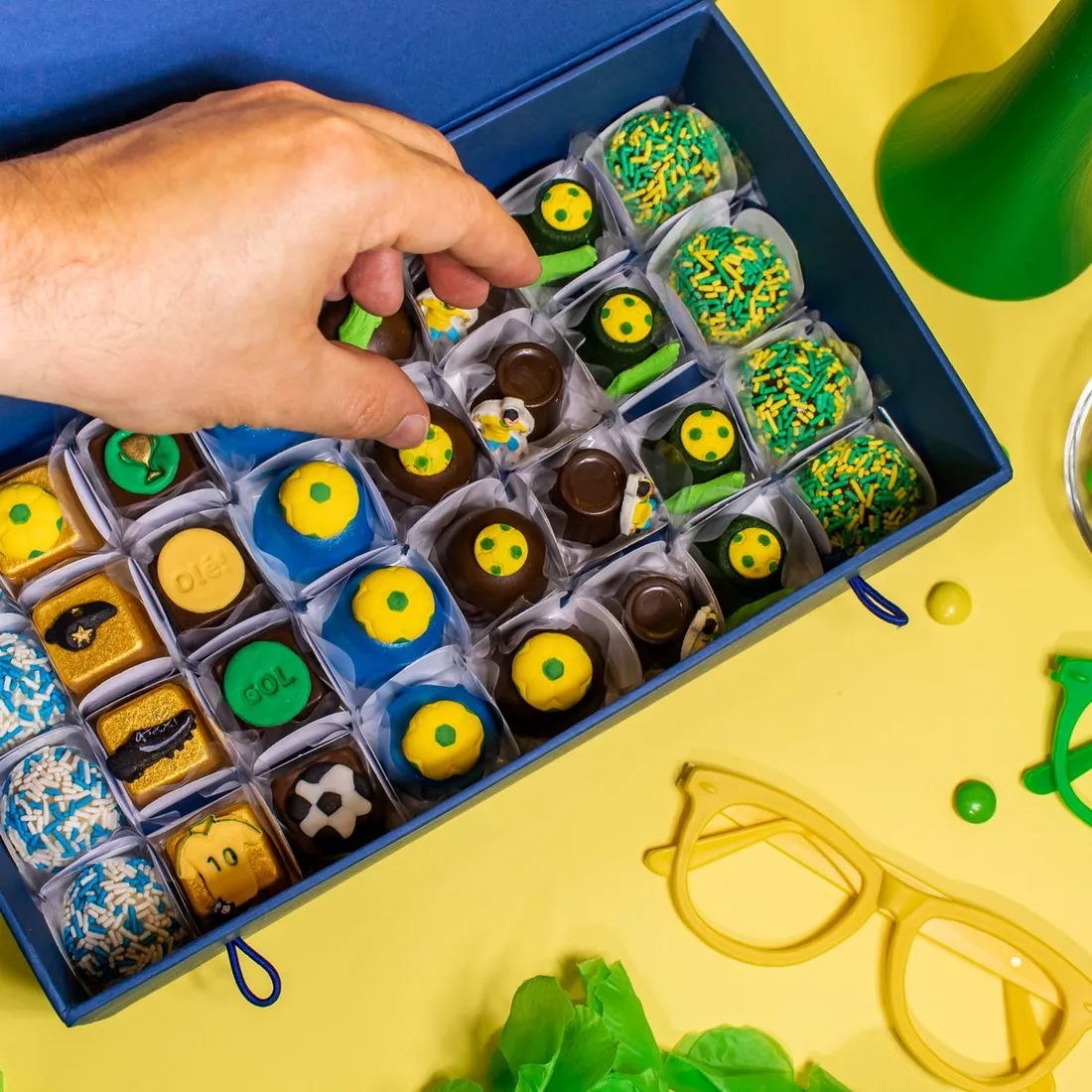 Caixa Caixa Gourmet temática de Copa do Mundo com brigadeiros decorados em formato de bola e cores verde, amarelo e azul.